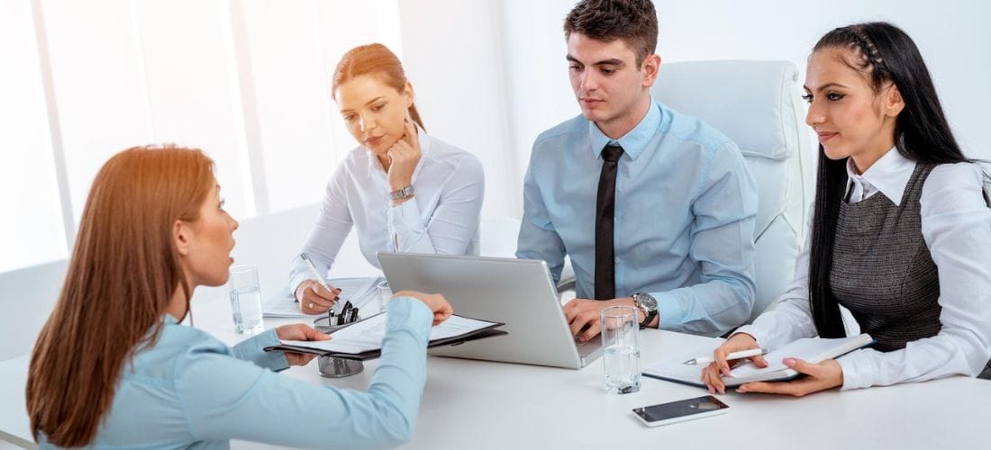 zdjęcie 4 osób siedzących przy biurku i komputerze